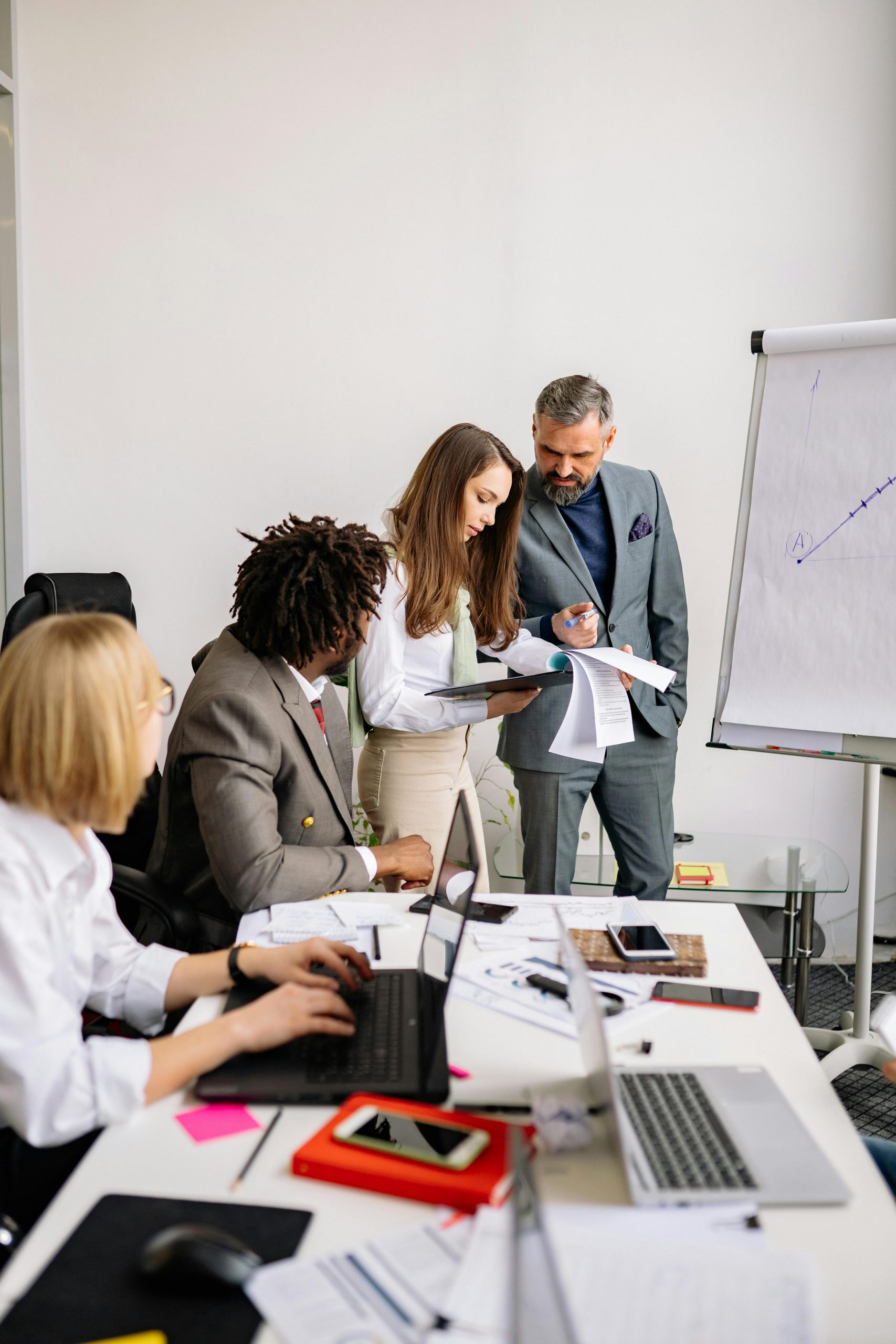 A diverse team collaborating in a modern office with laptops and a whiteboard.